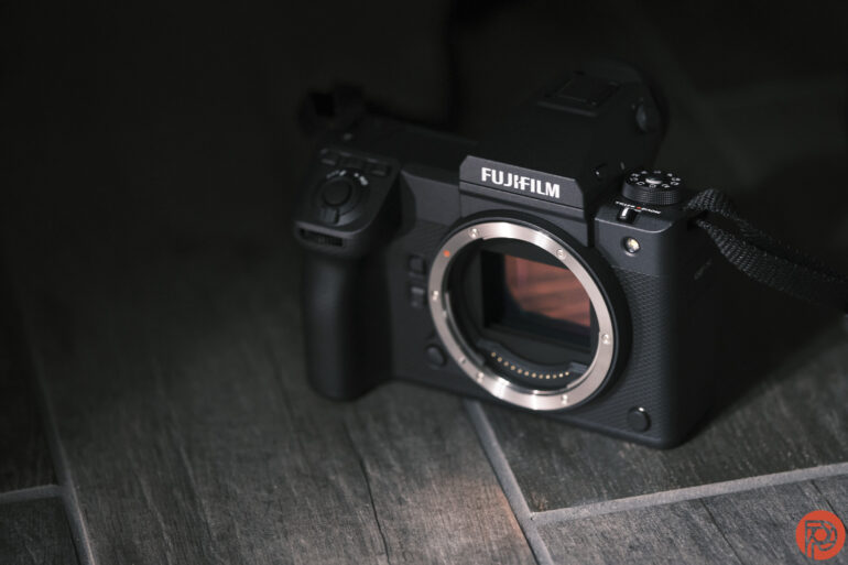 A Fujifilm camera body without a lens is placed on a dark wooden surface.