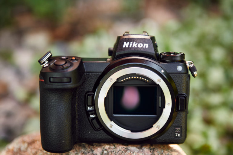 A Nikon Z7 II mirrorless camera body is placed outdoors on a rock, with a blurred green background.
