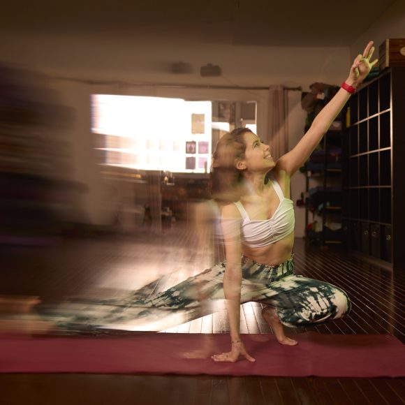Woman in motion practicing yoga indoors, stretching one arm upward on a red mat.