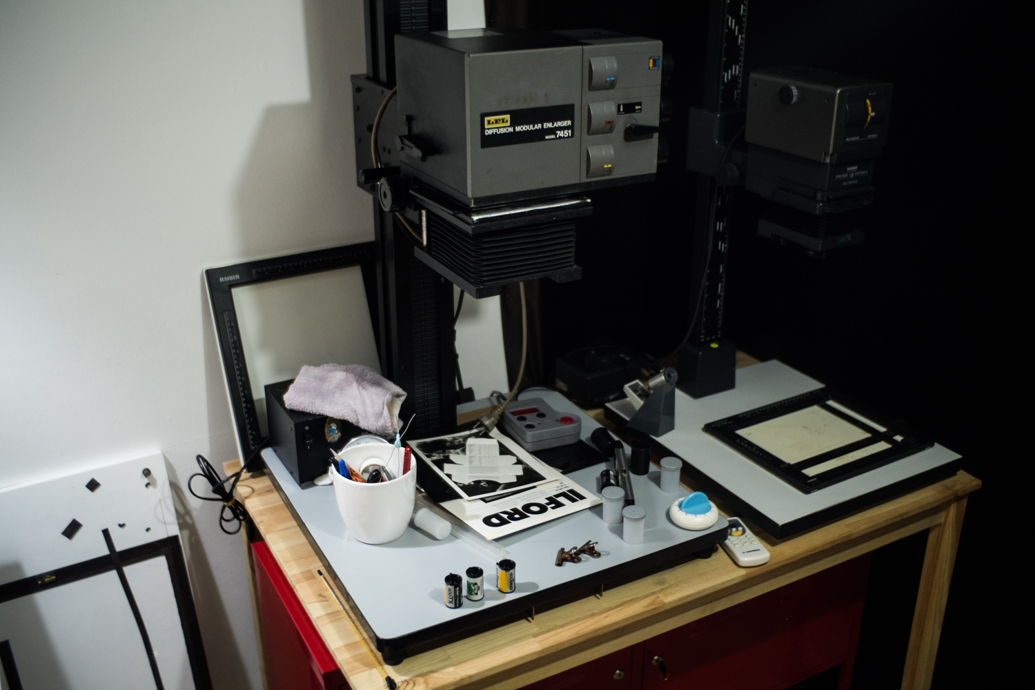 A film enlarger sits on a wooden table with photo development tools and supplies around it.