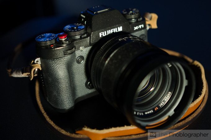 A Fujifilm X-T1 camera with a lens, resting on a leather strap in soft lighting.