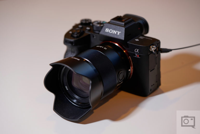 A Sony Alpha 7R digital camera with a lens attached, placed on a light surface.