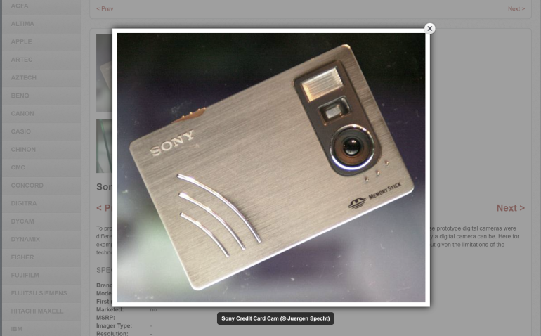 A silver Sony credit card-sized digital camera displayed at an angle against a dark background.